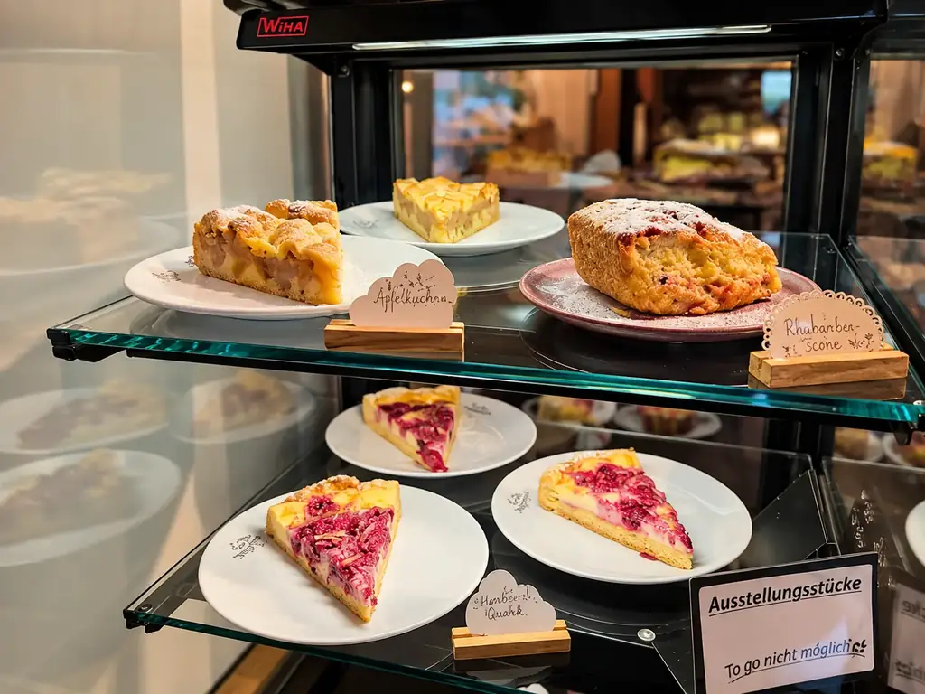 Kuchenvitrine mit Apfelkuchen, Rhabarber-Scone und Himbeer-Quarkkuchen, handbeschriftet